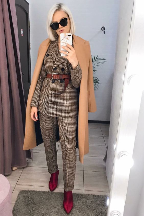 an elegant and formal fall work outfit with a grey plaid pantsuit, a brown belt, burgundy boots, a camel coat