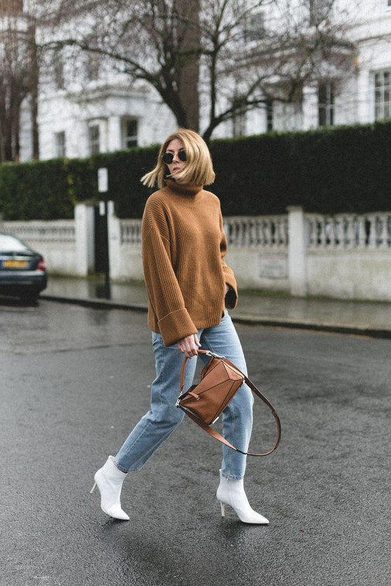 an oversized brown turtleneck sweater, blue jeans, white ankle booties and a brown geometric bag