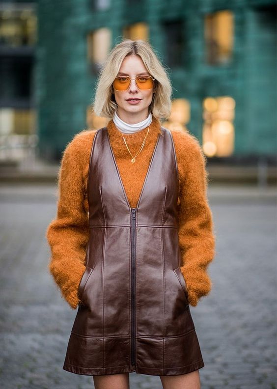 a bold fall outfit with an orange sweater over a white turtleneck, a burgundy metallic leather overall dress and a necklace