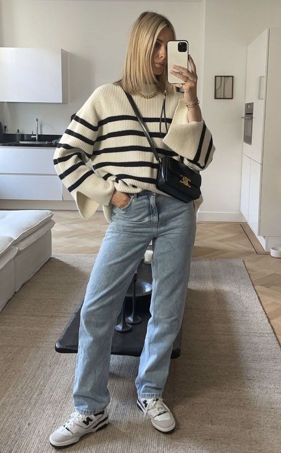 a comfortable fall outfit with a black and white stripe sweater, blue mom jeans, grey sneakers and a black bag