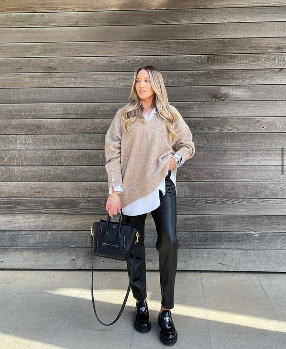 a cozy and chic work outfit with a white oversized shirt, a tan jumper, black leather trousers, black lacquer loafers and a bag