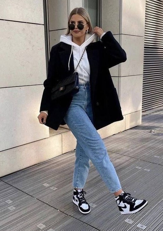 a stylish and contrasting fall work outfit with a white hoodie, blue high waisted jeans, black and white trainers, a black blazer and a black bag