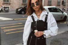 a white thin stripe oversized shirt, a black leather pinafore dress, a two-tone bag and a chain necklace