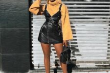 a yellow turtleneck, a black leather pinafore dress, black heels, a black bag and a black cap for the fall