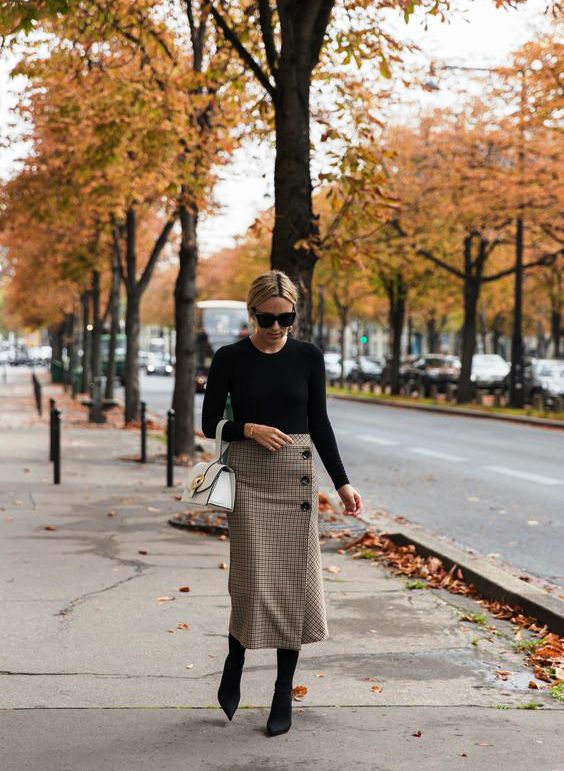 a black top, a plaid beige midi skirt, black sock boots and a white bag are a great combo for work