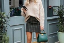 20 a blush oversized sweater tucked in a dark plaid mini skirt, creamy boots, an emerald bag