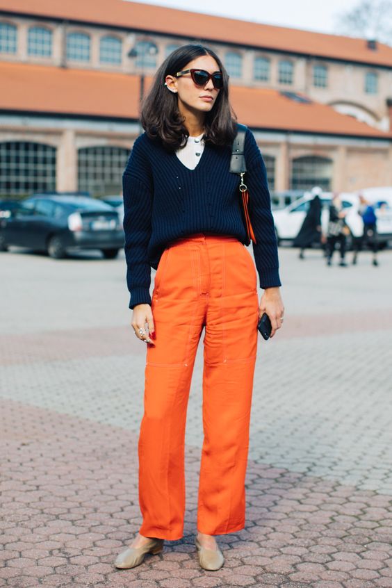 a cute and chic Thanksgiving outfit with a white button up top, a navy pullover, orange pants, grey shoes
