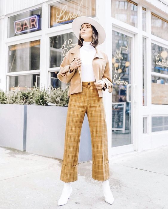 a white turtleneck, mustard plaid trousers, a tan jacket, white boots and a creamy hat