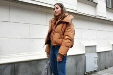 a beautiful winter outfit with an amber sweater and a matching cropped puffer jacket, blue cropped jeans, brown boots and a grey bag