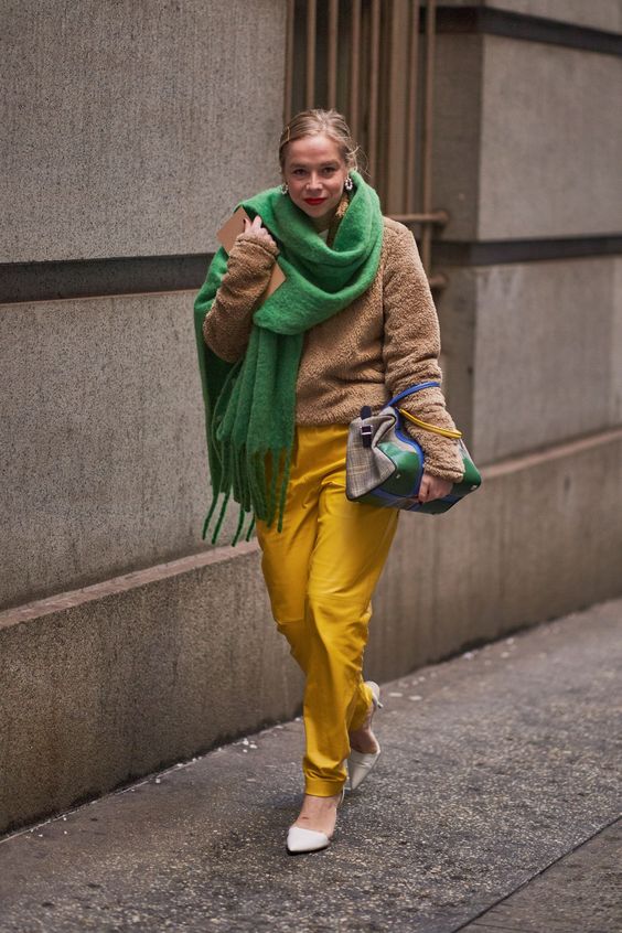 a beige plush sweater, yellow trousers, white shoes, an oversized green scarf and a two tone bag