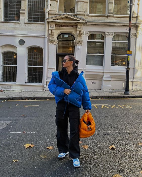 a black hoodie, black jeans, blue sneakers, a bold blue cropped puffer jacket and an orange puffer bag