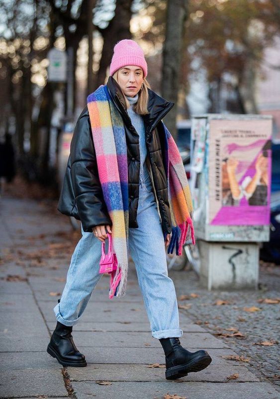 a blue sweater and blue jeans, a black leather puffer jacket and boots, a colorful scarf and a pink beanie for winter