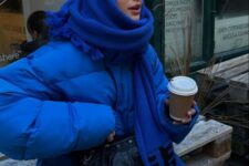 a bold winter outfit with an electrc blue puffer jacket and an oversized scarf, leaher pants and a small bag