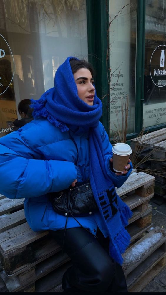 a bold winter outfit with an electrc blue puffer jacket and an oversized scarf, leaher pants and a small bag
