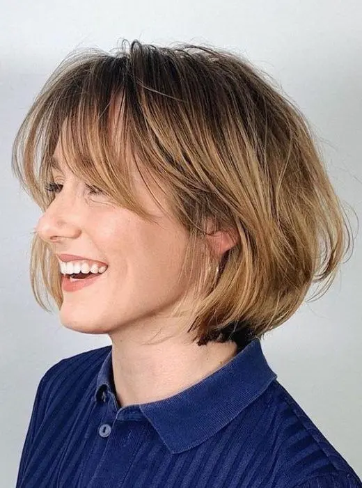 a chin-length bob with honey blonde balayage and long curtain bangs, curved ends and a bit of volume