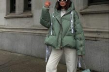 a cool winter outfit with a white turtleneck, white jeans, grey trainers, a grene puffer jacket and a green bag