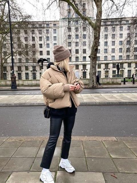a cozy winter look with a black hoodie, black leather pants and a bag, white trainers, a beige puffer jacket and a brown bag