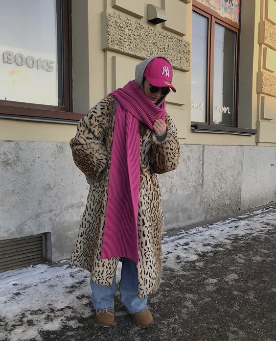 a faux leopard midi coat, blue jeans, brown ugg boots, a pink scarf and a pink cap for a comfy and bold winter look