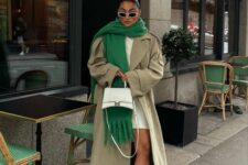 a neutral mini dress, black chunky boots, a griege coat, a white bag and an oversized green scarf with fringe