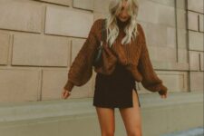 a sexy Thanksgiving outfit with a rust-colored oversized sweater, a black mini, creamy cowboy boots and a black bag