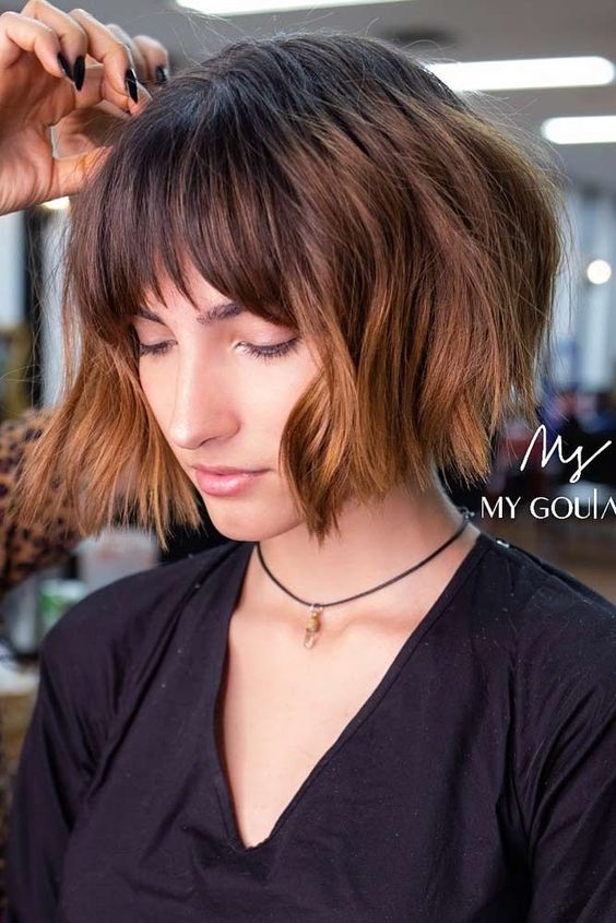 A shaggy chin length bob with caramel balayage and wispy bangs plus waves is a stylish idea with cool highlights