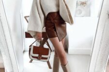 a sophisticated Thanksgiving outfit with a creamy chunky knit sweater and bell sleeves, a brown knot mni skirt, tan knee boots and a two-tone bag
