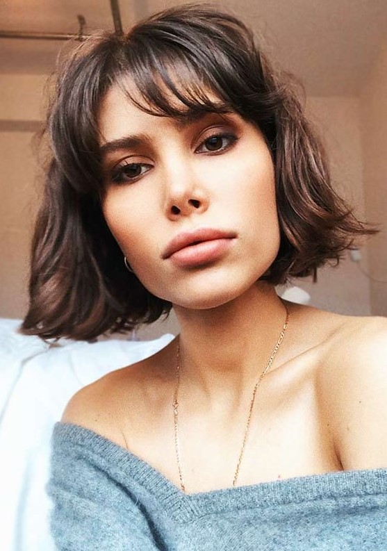 A stylish dark burnette chin length bob with wispy bangs and messy waves is a cool idea to rock right now