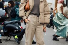 a stylish winter outfit with a taupe t-shirt, beige trousers, a beige puffer jacket, white sneakers and an amber bag