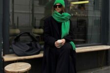 a total black look with pants and a sweater, sneakers and a coat, a bold green scarf and a beanie, a large black bag