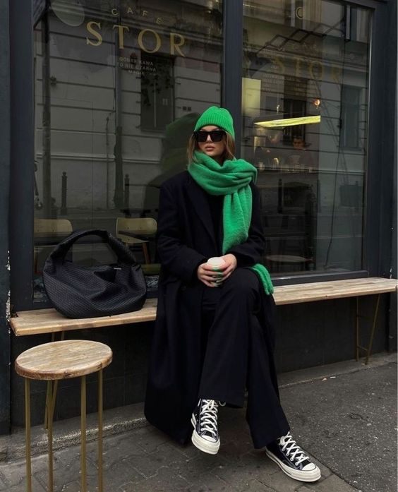 a total black look with pants and a sweater, sneakers and a coat, a bold green scarf and a beanie, a large black bag