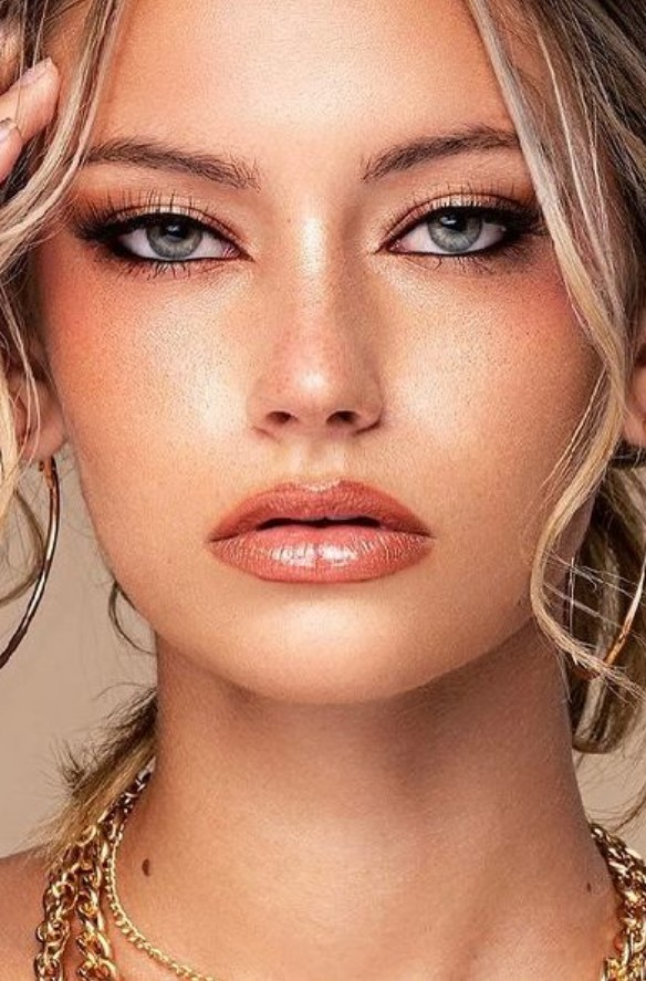 a warm toned siren eye makeup with a shiny coral lip, a touch of blush, pink siren eyes and highlighter
