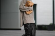 an oversized grey sweater, black leather pants, brown loafers and a beige clutch bag for winter