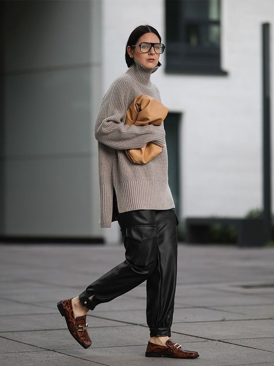 an oversized grey sweater, black leather pants, brown loafers and a beige clutch bag for winter