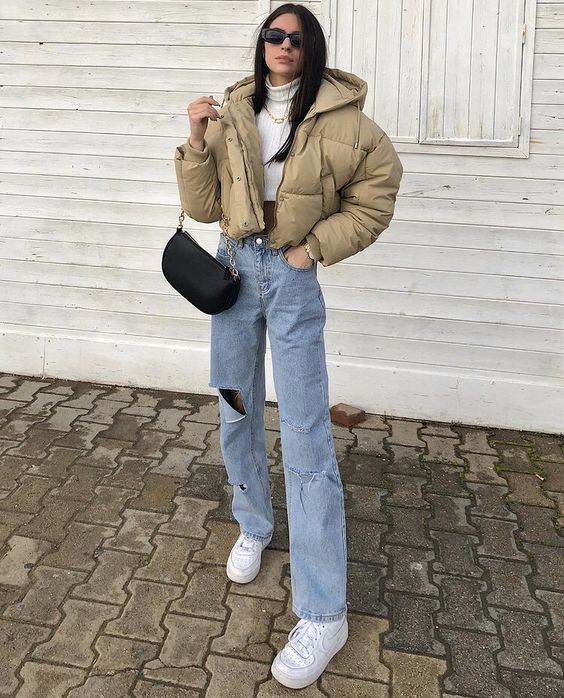 blue ripped jeans, a white sweater and sneakers, a beige cropped puffer jacket and a black bag for winter
