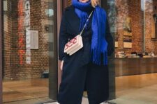 white jeans, a black midi coat, a bold blue scarf, a light blue beanie, red boots and a white and red bag