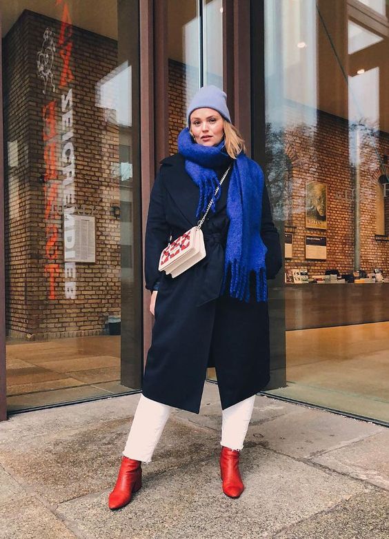 white jeans, a black midi coat, a bold blue scarf, a light blue beanie, red boots and a white and red bag