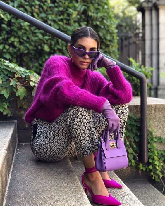a bright outfit with a magenta chunky knit sweater and lace up shoes, printed pants, a purple bag and gloves is amazing