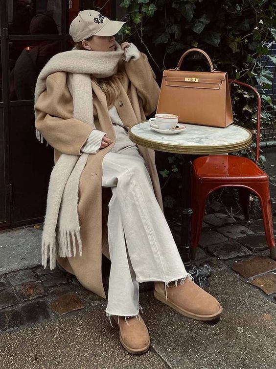 an all-neutral winter look with a sweater, jeans, beige bots, a beige coat, a creamy scarf and a cap plus a beige bag