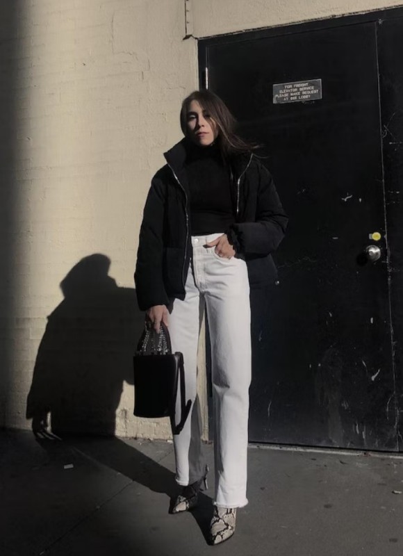 a monochromatic winter look with a black turtleneck, a puffer, a bucket bag, white jeans and snakeskin boots