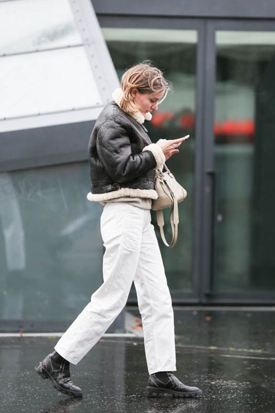 a winter outfit with white jeans, black boots, a black and white cropped aviator and a nude bag