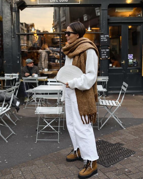 a white oversized sweater, white jeans, an oversized brown scarf and brown tracking boots, a white clutch