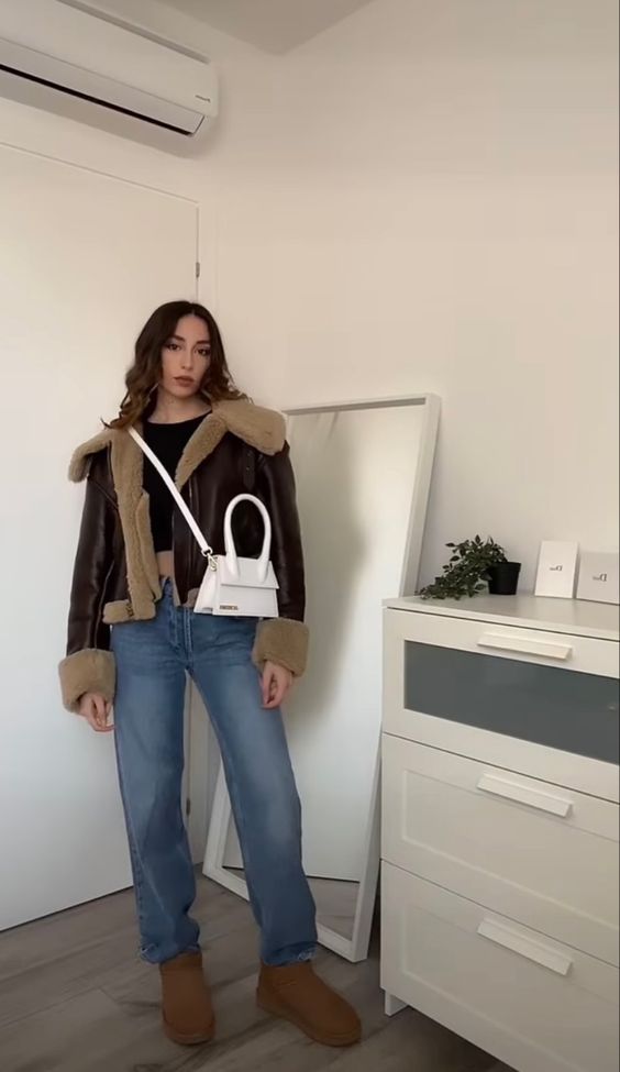 a black crop top, blue jeans, brown ugg boots, a brown cropped shearling jacket and a white bag