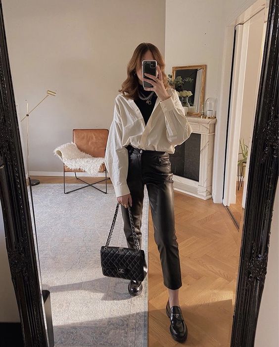a black turtleneck, a white shirt, black leather pants, black loafers, a black bag and layered necklaces for a layered winter work look