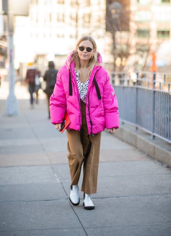 a bold winter outfit with a spotted top, brown pants, white Chelsea boots, a hot pink puffer jacket
