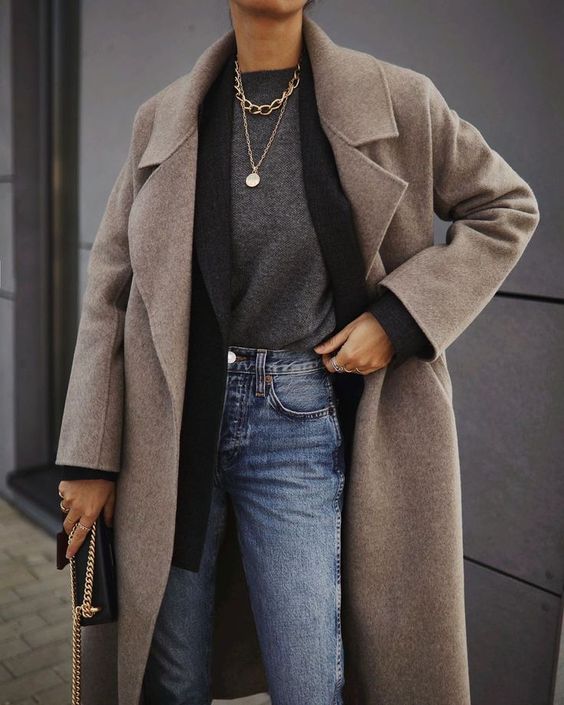 a comfy layered winter work look with a grey top, a black oversized blazer, blue jeans, a beige coat and a black bag plus layered necklaces