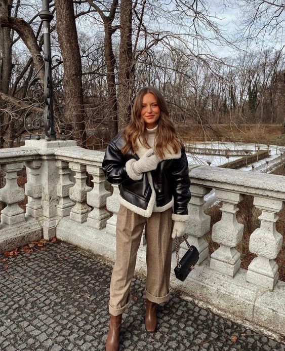 a cozy and chic winter outfit with a white turtleneck, beige trousers, brown boots, a black aviatora and white mittens