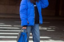 a cozy sporty look with a black hoodie, blue jeans, black sneakers, a bold blue puffer jacket and a matching bag