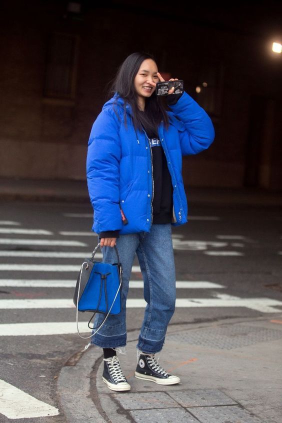 a cozy sporty look with a black hoodie, blue jeans, black sneakers, a bold blue puffer jacket and a matching bag