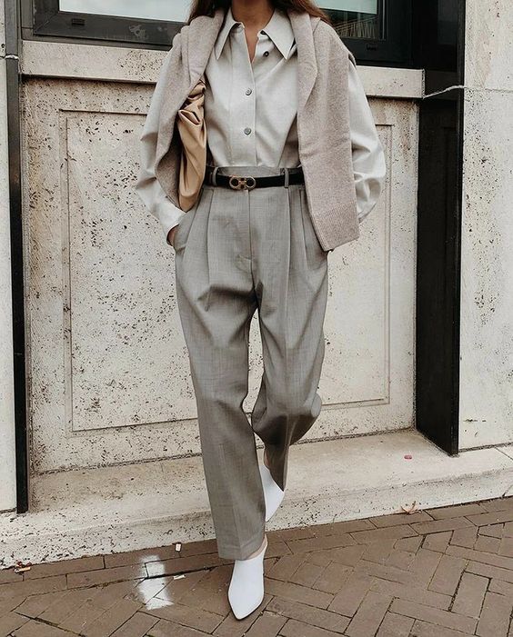 a grey oversized shirt, grey high waisted pants, white shoes, a grey jumper over the shoulders and a tan bag