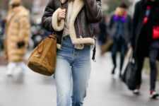 a neutral top, blue jeans, burgundy boots, a brown cropped shearling jacket and a beige bag